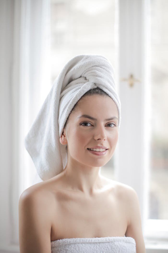 Young woman with towel wrapped around her head in a bright bathroom setting.